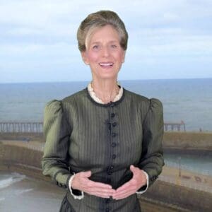 A woman with short hair stands by the seaside, smiling warmly.